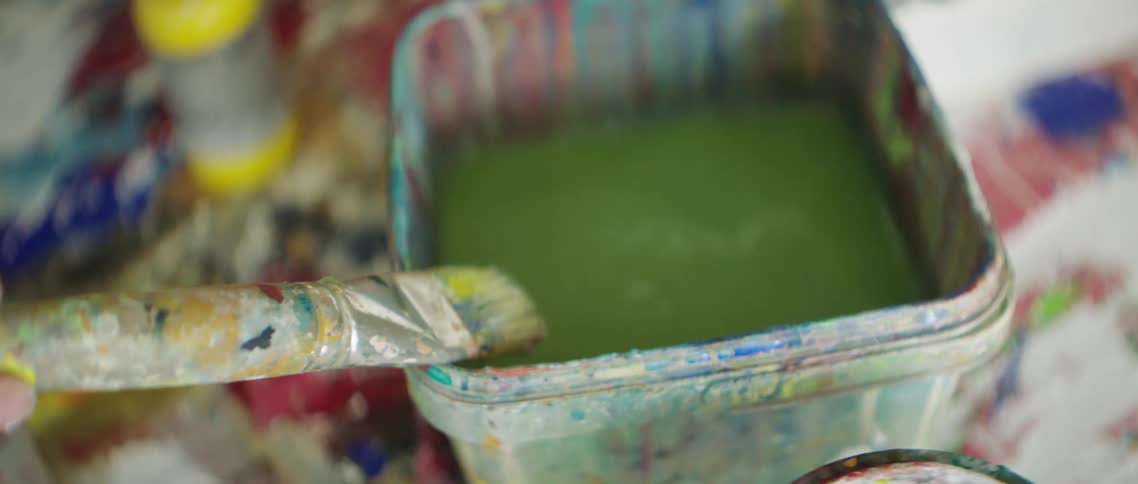 A white woman cleans a paint brush in a bucket of dirty water