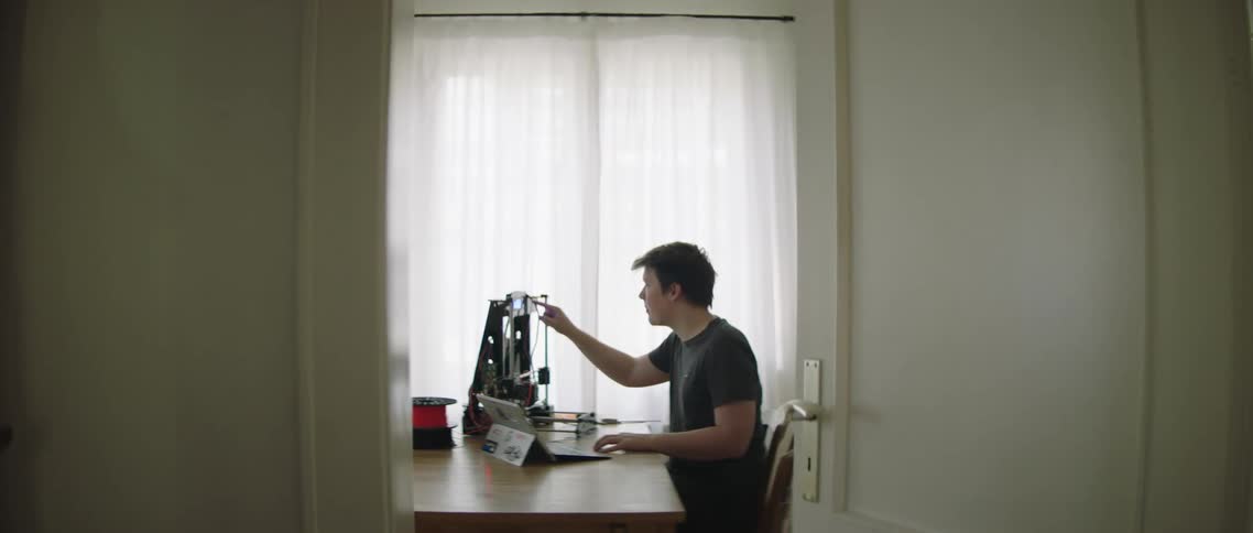 A man sits at a table and uses a 3d printer