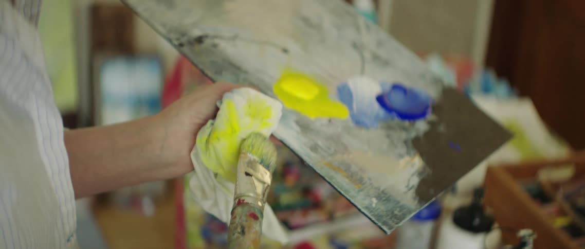 A painter removes excess yellow paint from a paintbrush