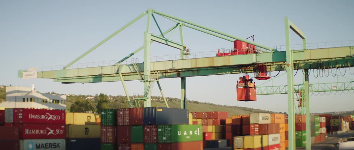 Crane unloading shipping containers from a cargo boat in a pier at sunrise