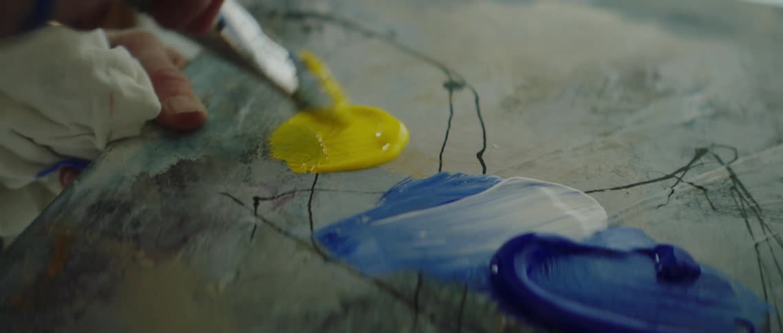 A white female artists brushes yellow paint on a palette