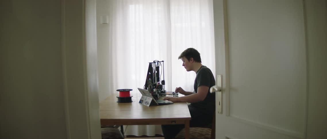 A white teenager sits a dining room table and works on a piece of technology