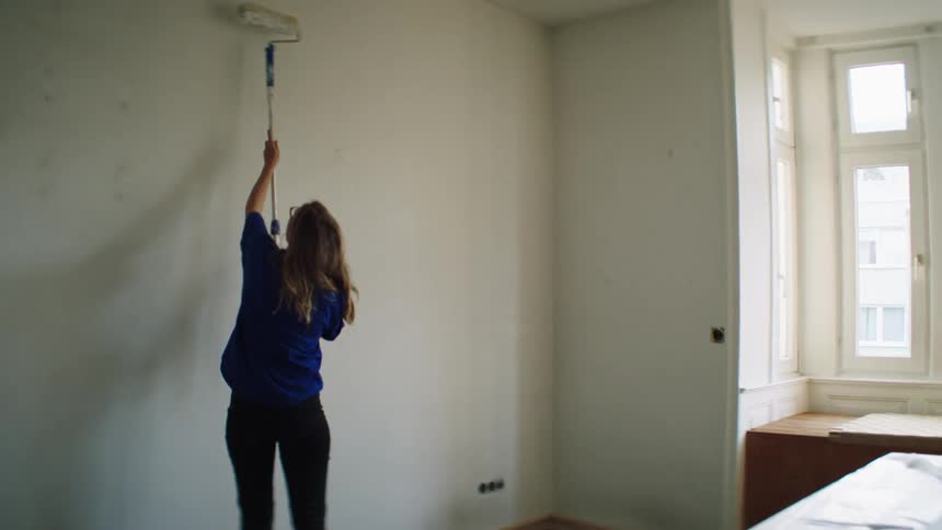 A woman paints a wall in her home