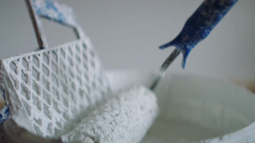 A person uses a roller in a bucket of white paint