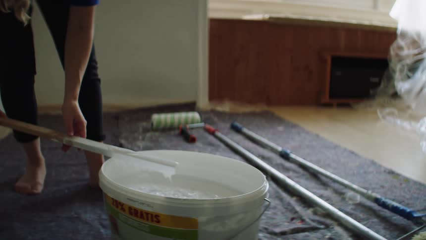 A woman stirs a large bucket of paint with a stick