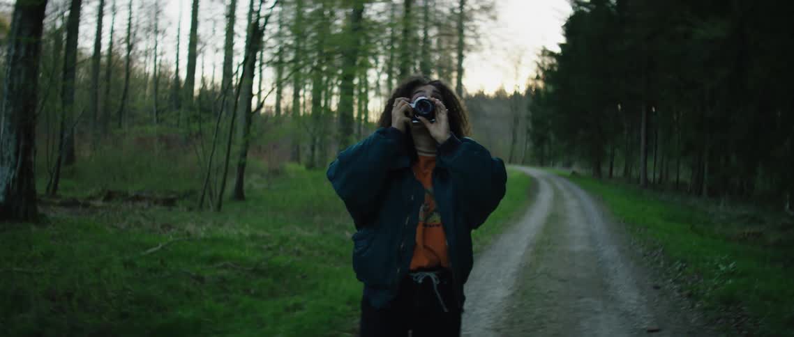 Photographer walks along country road through woods taking pictures