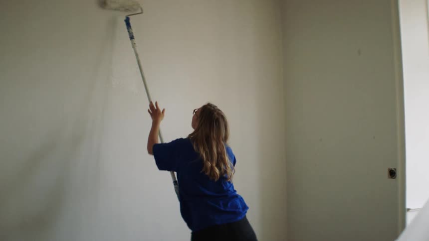 Woman loads paint onto roller and begins painting wall