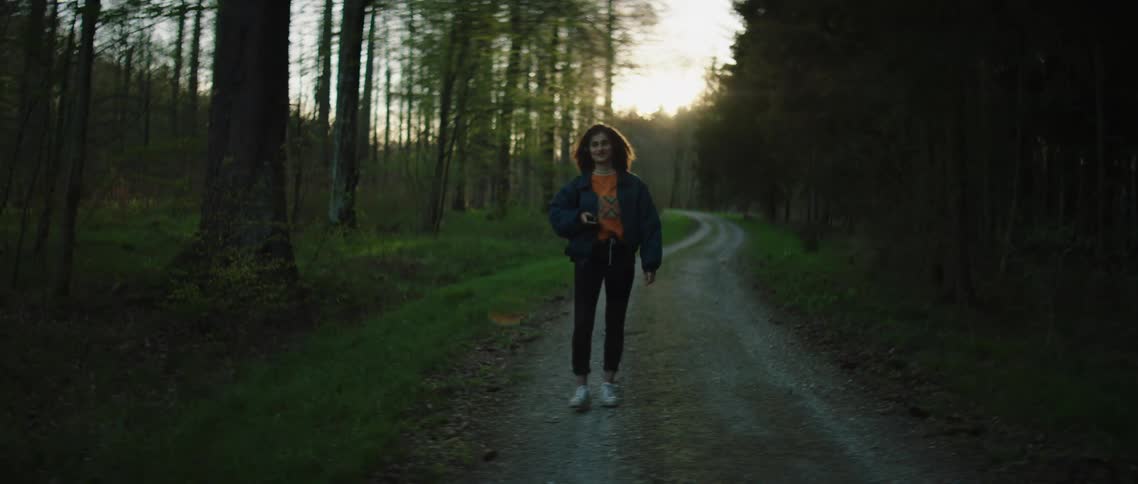 Young woman walking on gravel driveway through woods