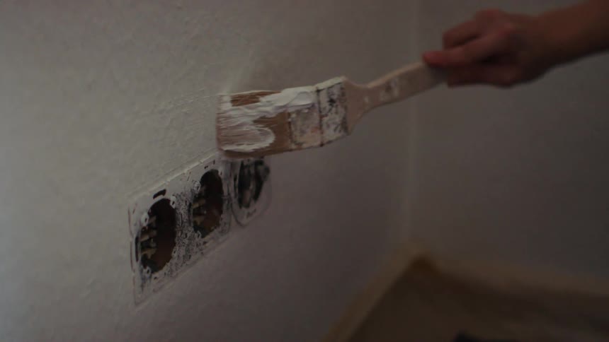 Person brushes white paint around outlet on wall