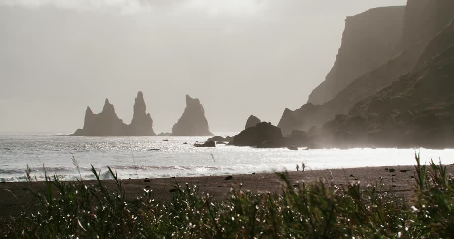 People walk on the beach as ocean waves crash and splash on shore on a windy day