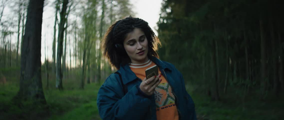 A woman outside with headphones dancing and looking at a smart phone