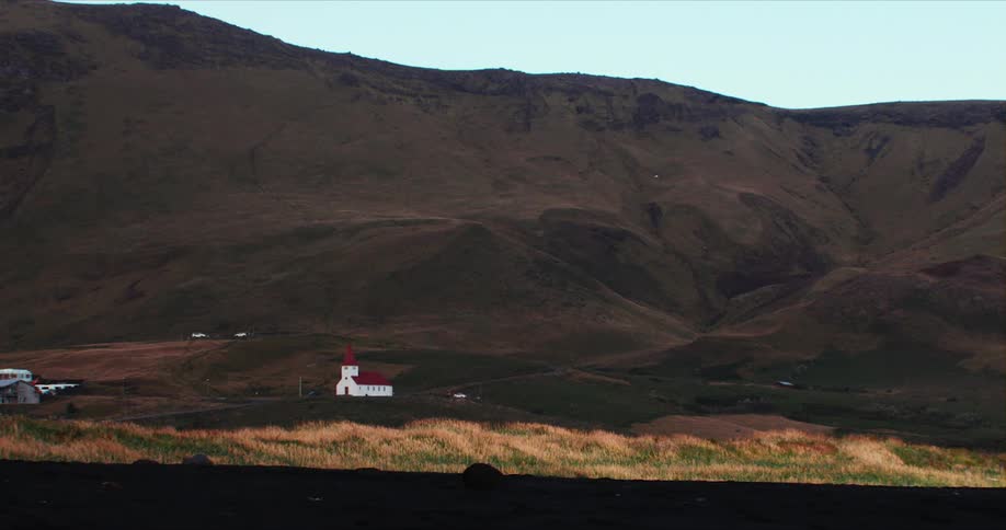 Church with a red roof sits near the mountains under a blue sky