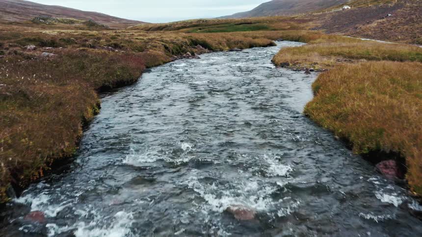 A stream running through a hilly countryside on a rainy day