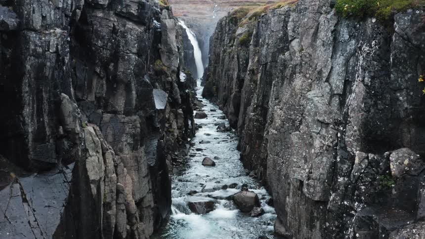 A waterfall feeds a river and rapids in a deep canyon