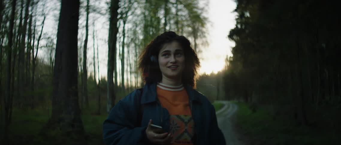 A woman walks backwards on a trail listening to music