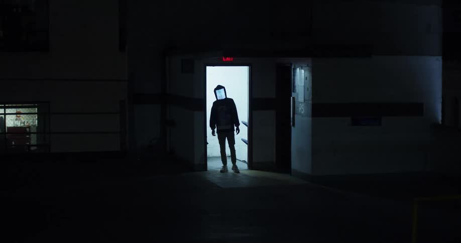 Silhouetted figure wearing digital mask showing static stands in doorway of empty building