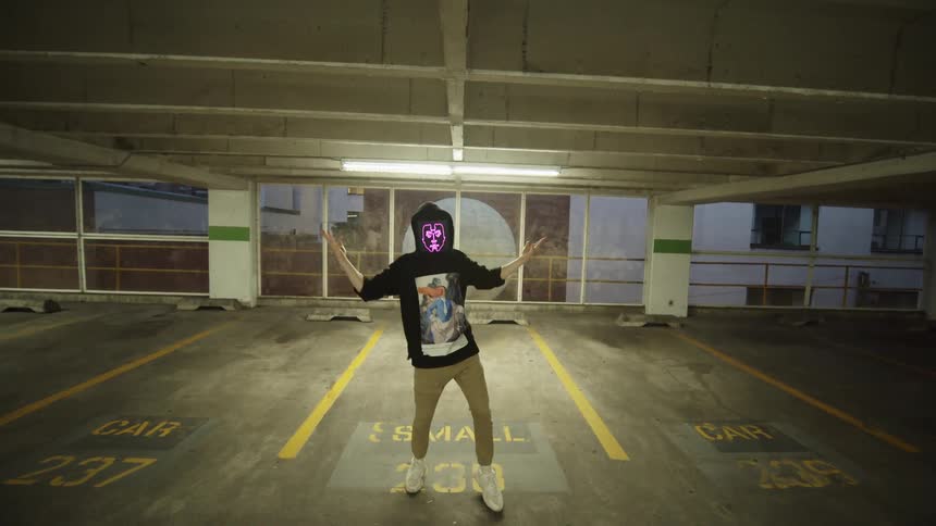 A white rapper with a digital screen for a face raps in an indoor garage