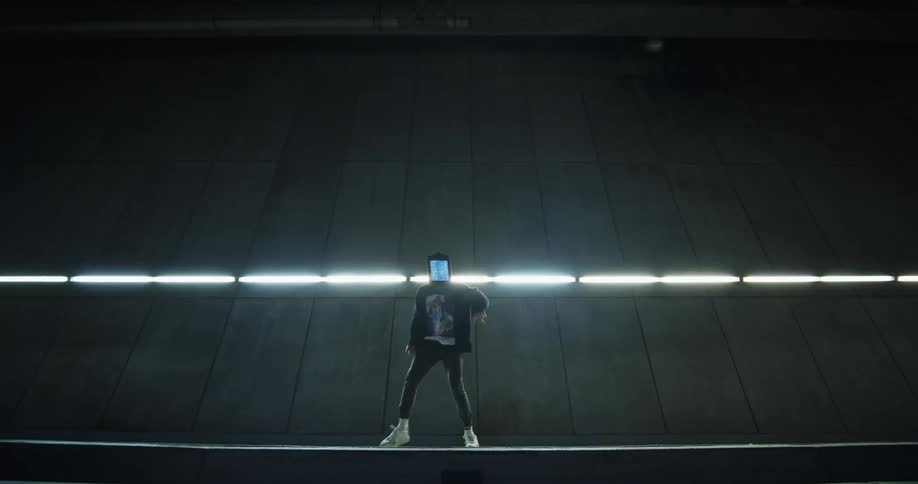 A person with a face covering dances in fast motion in front of a wall