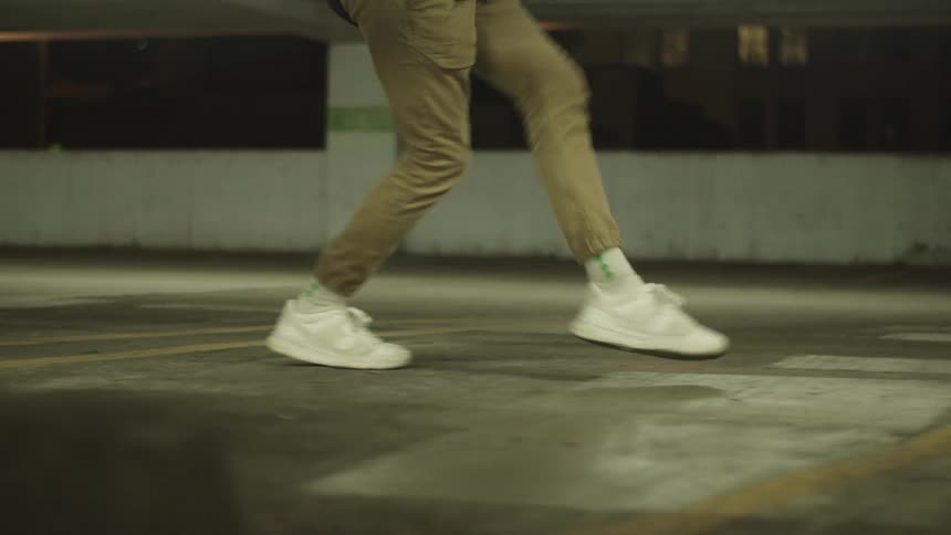 Male performs creative dance steps as he moves through an empty parking garage alone