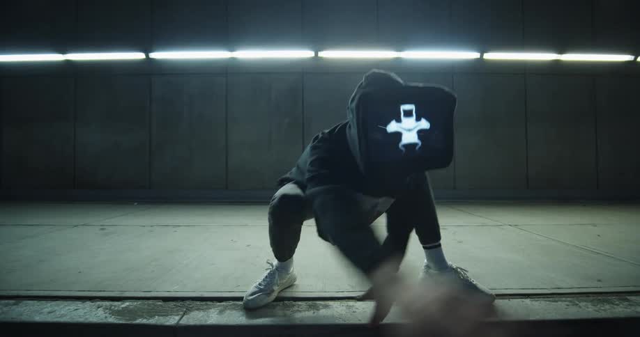 A person wearing a digital display as a mask dances in a squatted animal like position
