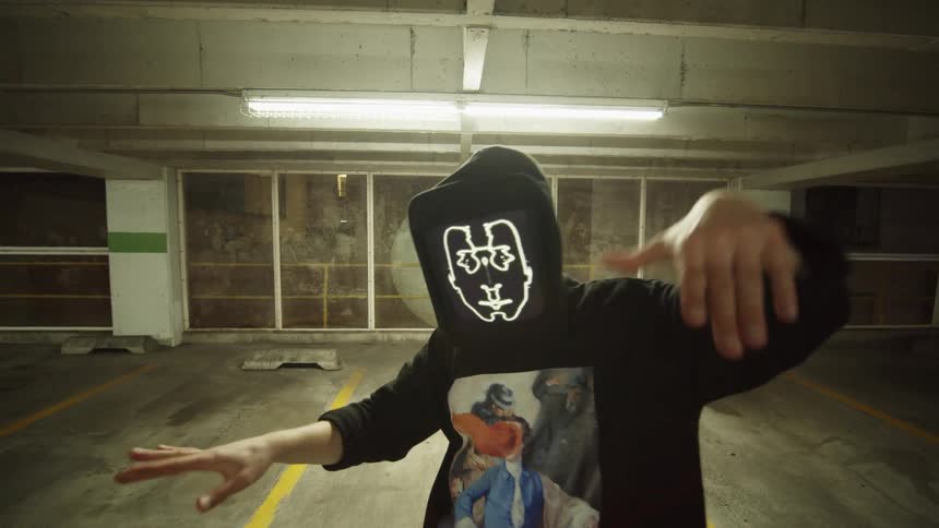 A masked man dances in a parking garage