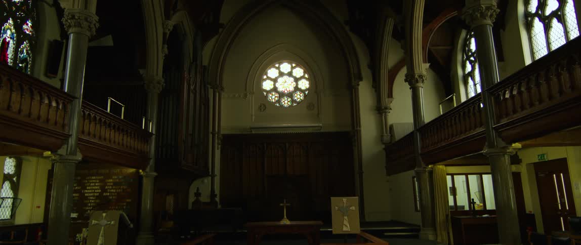 Interior of an empty church dimly lit by the sun through stained glass window