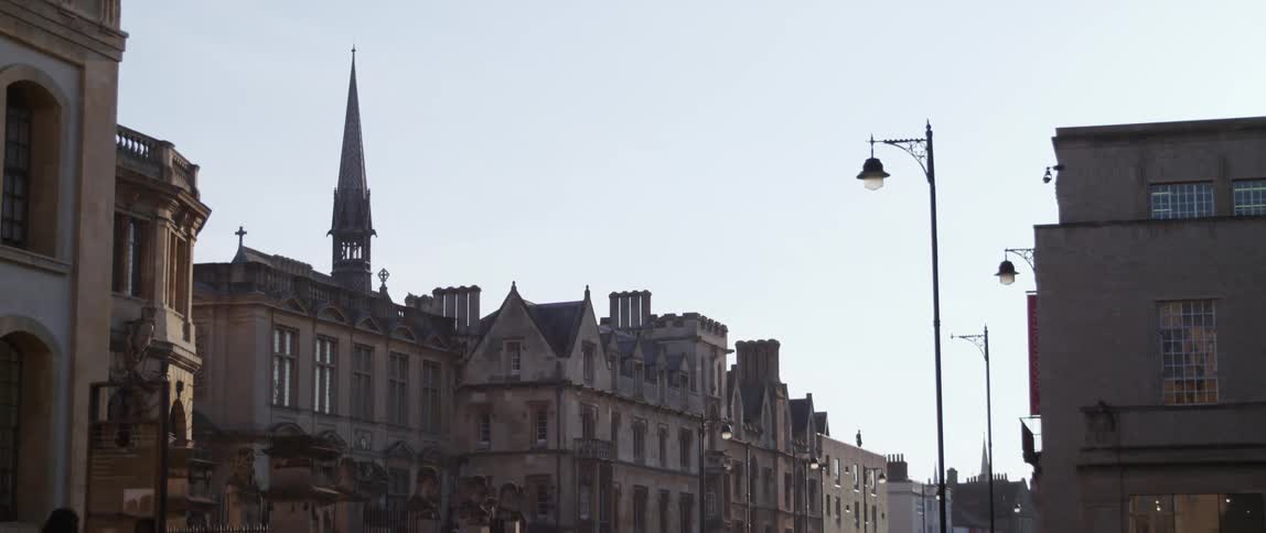 People walk and bike down a city street in Oxford England as cars drive by