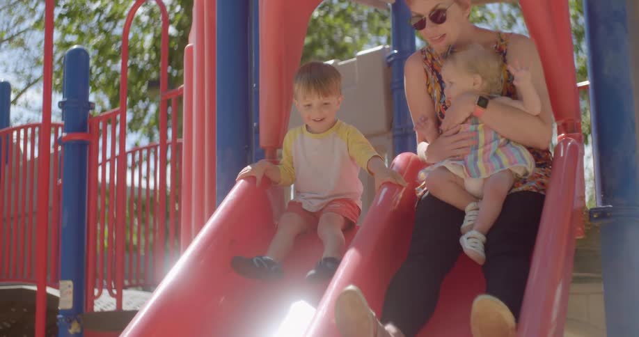 Mother sliding down slide with her children at a park