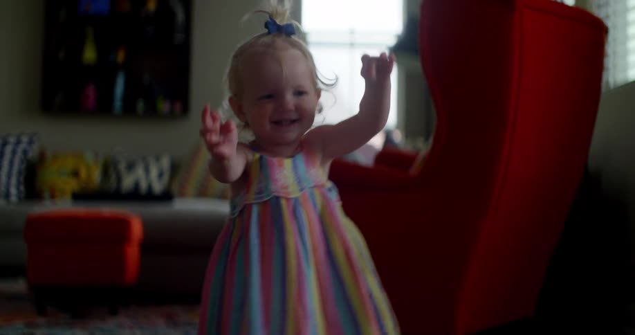 Female toddler begins walking with an unsteady gait across the room as she smiles and reaches out in front of her