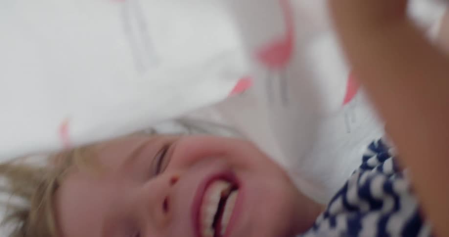 A white child laughs as he rolls around underneath a bed sheet
