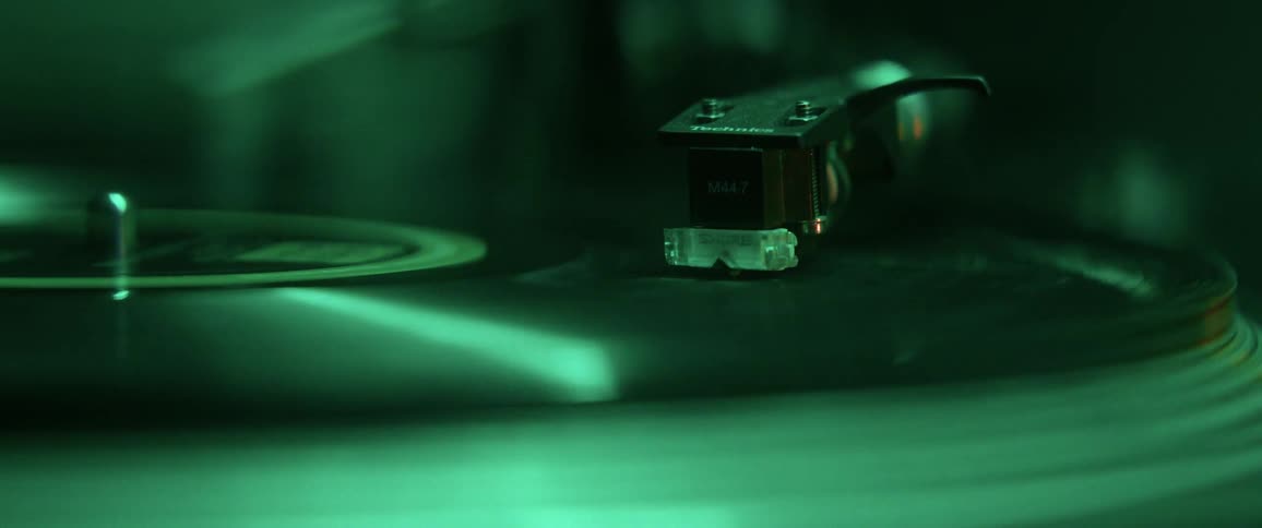 The needle of a record player on a spinning vinyl record under colored lighting