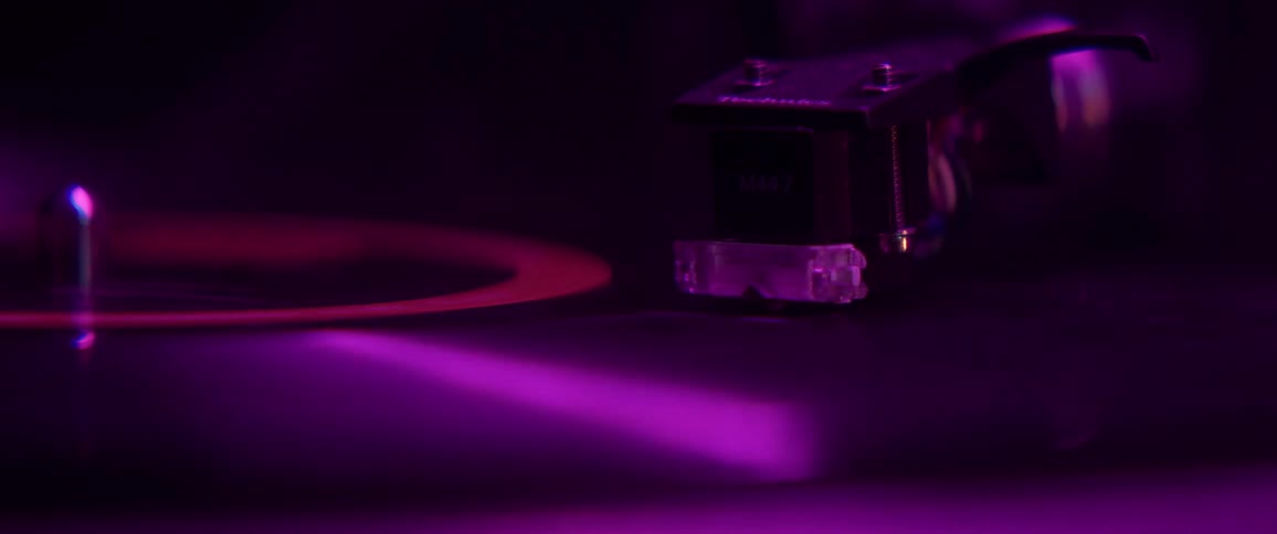 Record player needle on spinning record under color changing light