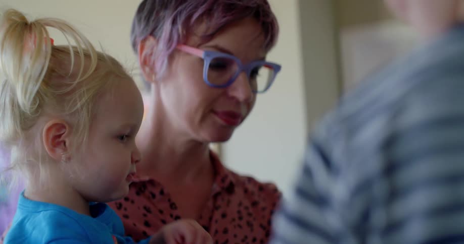 Woman with short hair and colorful glasses talks to her children in the kitchen