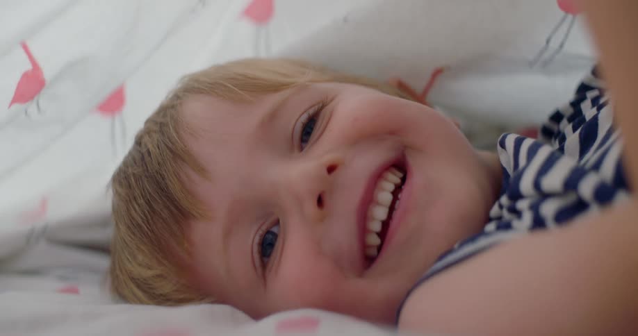 A boy laying in bed smiling under the covers