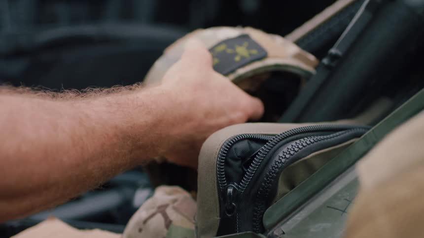 A man picks up a military helmet from a pile with his weapon and gear