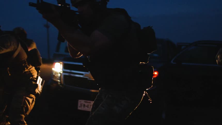 A group of military soldiers hold their weapons at sight and walk away from a vehicle