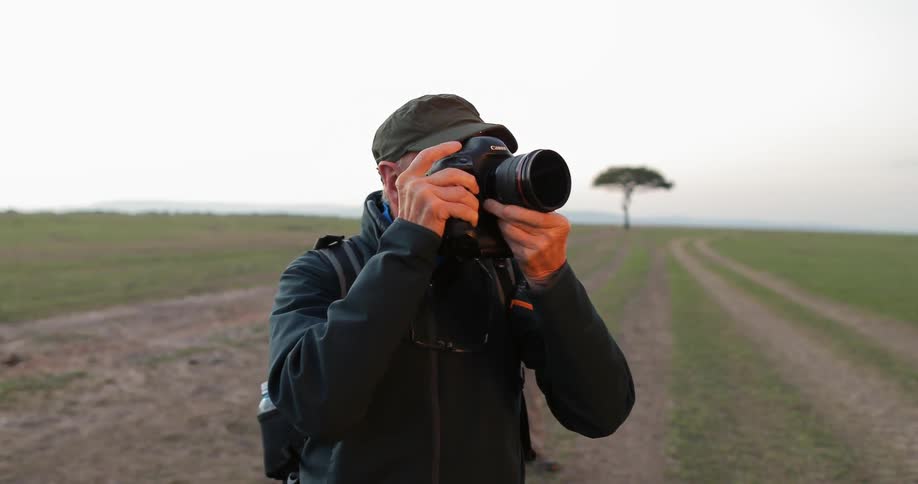 A man is photographing while standing on a large grass field