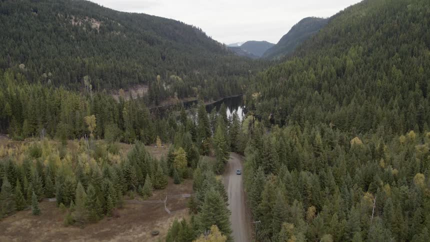 A truck drives down a remote road near a lake in a mountain valley