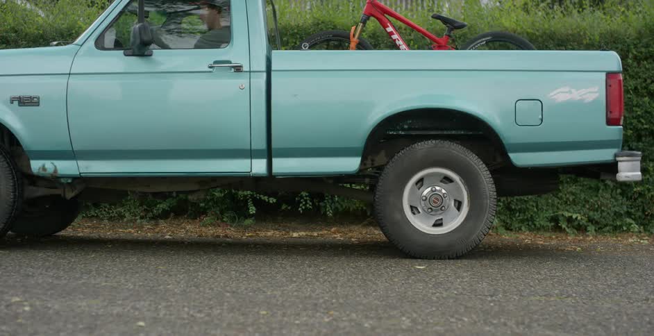 A man with a bike in the back of his truck drives away