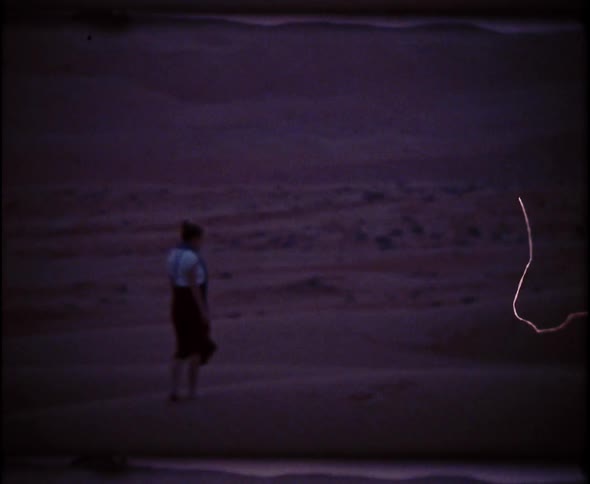 Woman walks in the desert at sunset