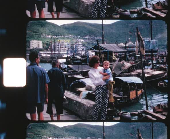 A white woman holds a baby by a marina as pedestrians walk by