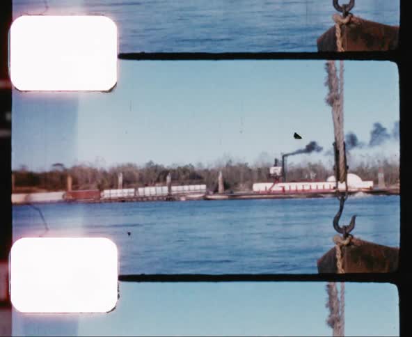 A boat floats on a body of water as a train moves across tracks on the shore