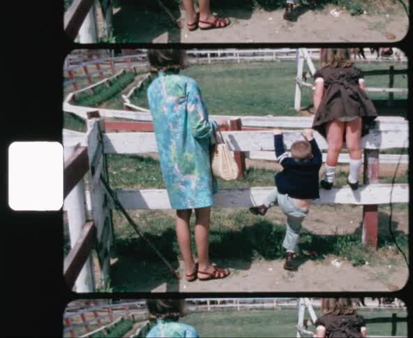 A mother and two children watch two people ride horses around an oval track