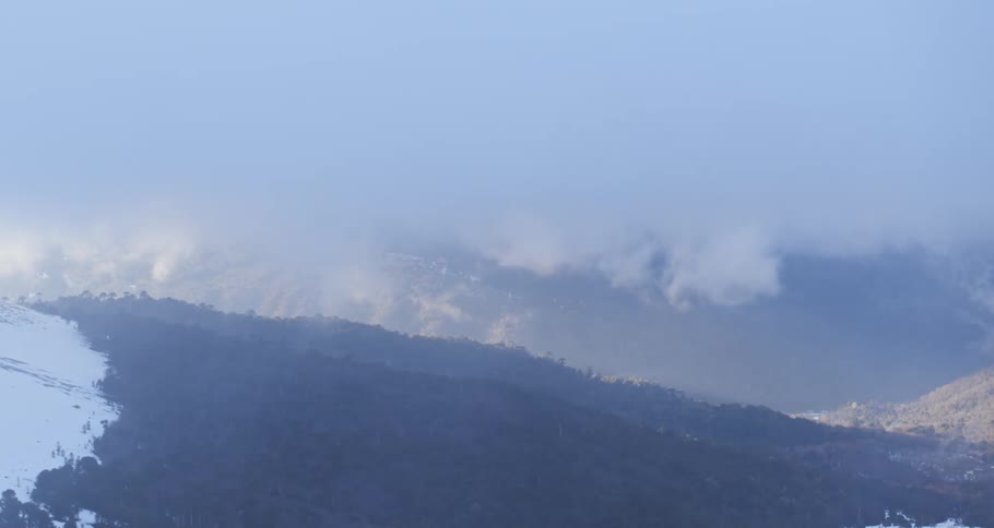Aerial push through clouds on a snowy mountain forest