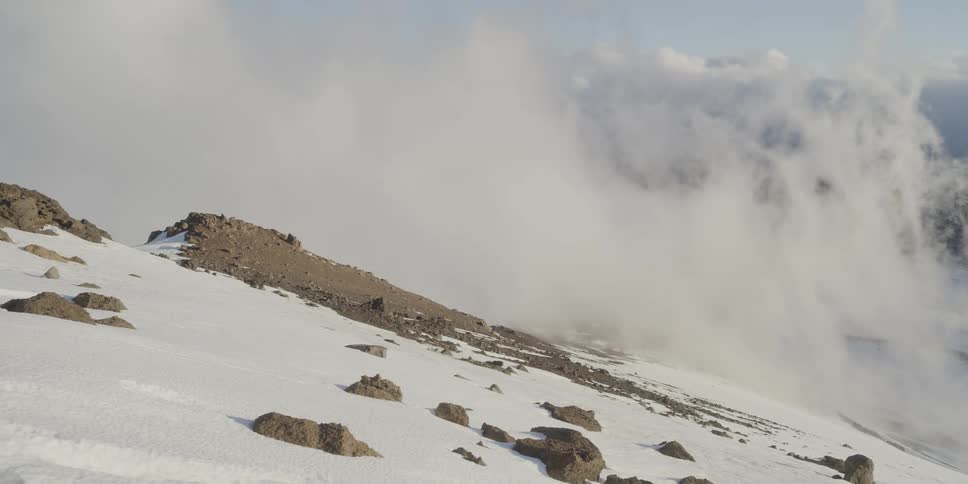 Clouds move across a rocky mountain slope covered in snow
