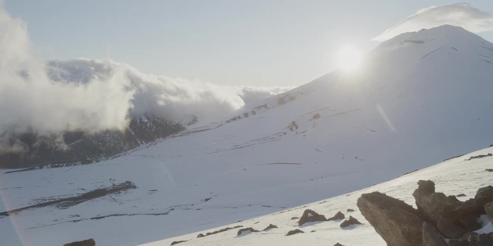 The sun peeks from behind a snow covered mountain