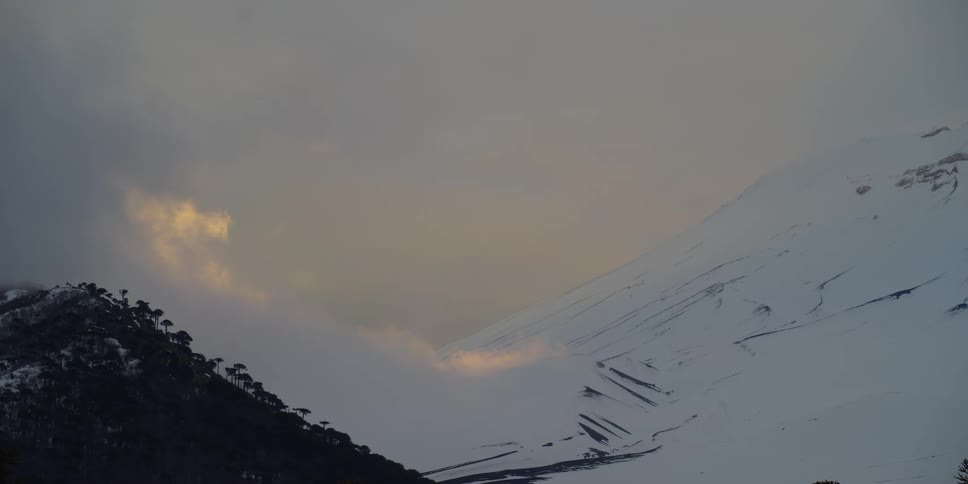 Clouds hang low over the slope of a mountain range at sunset