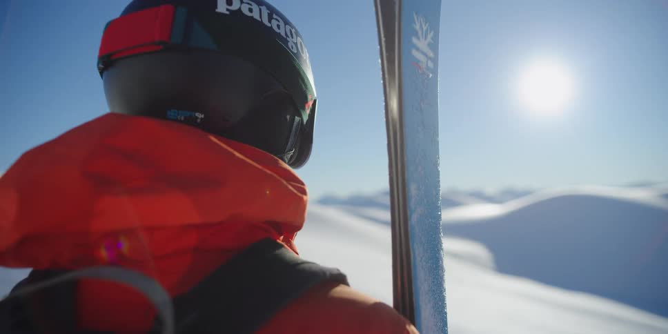 A skier stands on a snow covered mountain holding skis