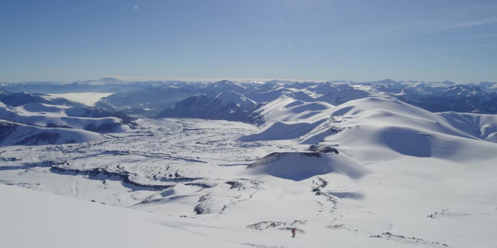 Wide shot of mountain landscape in winter with person skiing down slope