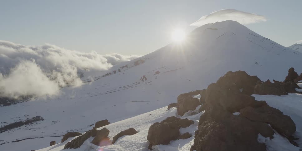 The sun peeks around a snowy volcano